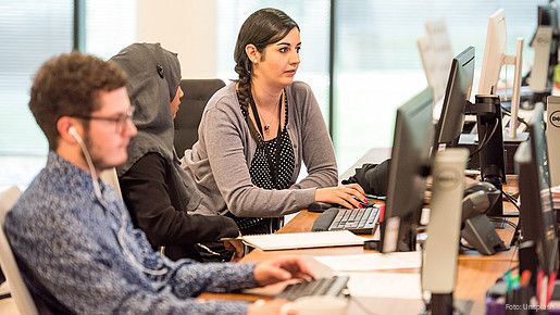 Blick in ein Büro auf einen jungen Mann und zwei Frauen, eine von ihnen trägt ein Kopftuch. Alle schauen auf ihre Computer-Bildschirme