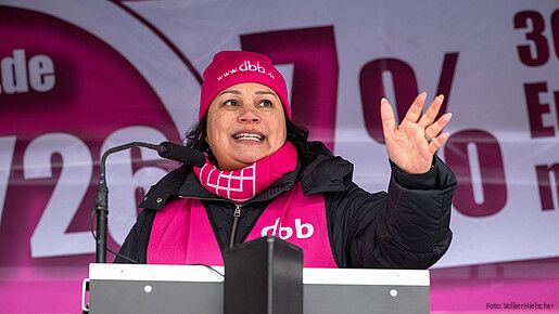 Eine Frau steht auf einer Bühne hinter einem Rednerpult und spricht in das Mikrofon