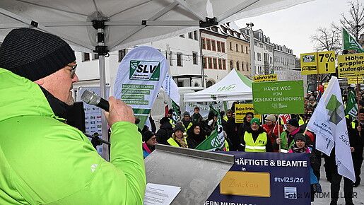 Ein Mann spricht auf einer Bühne vor einer Demonstration