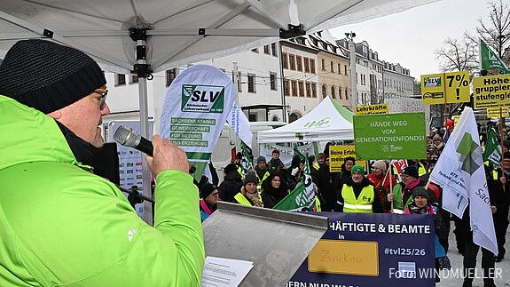Ein Mann spricht auf einer Bühne vor einer Demonstration