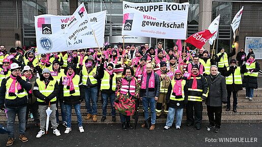 Eine Gruppe Menschen demonstriert mit bunten Bannern und Fahnen auf den Stufen eines Krankenhauses