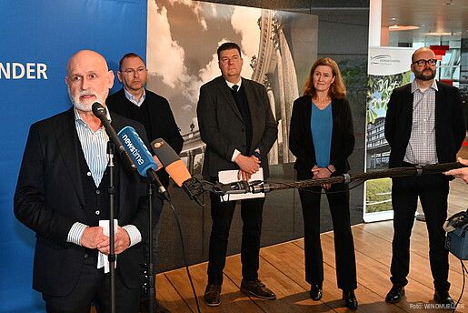 Ein Mann steht vor mehreren Mikrofonen und gibt ein Interview