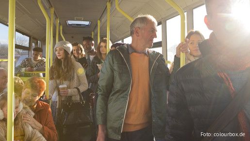 Blick in den Innenraum eines Busses auf stehende und sitzende Passagiere aus allen Altersgruppen
