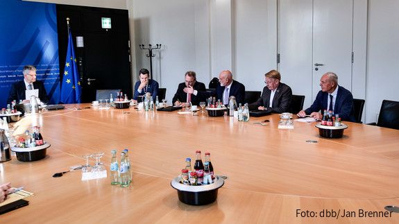 Mehrere Menschen in Anzügen sitzen an einem großen runden Tisch und diskutieren miteinander