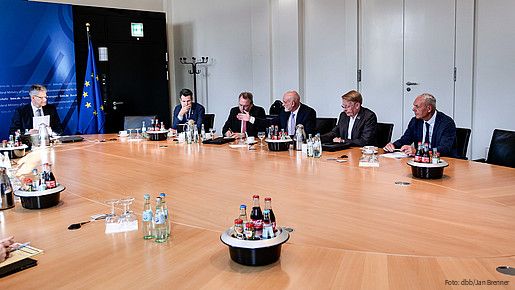 Mehrere Menschen in Anzügen sitzen an einem großen runden Tisch und diskutieren miteinander