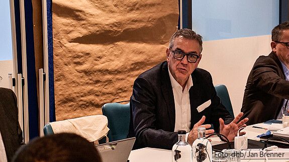 Ein Mann sitzt an einem Tisch in einem Seminarraum und diskutiert.