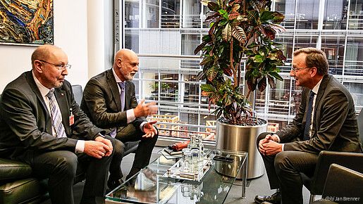 Drei Männer sitzen in einem Büro und diskutieren miteinander