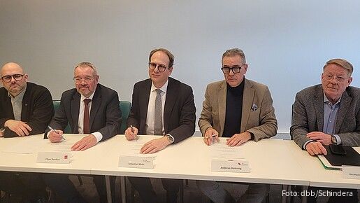 Mehrere Männer sitzen an einem langen Tisch und unterzeichnen Verträge