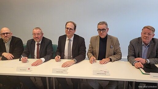 Mehrere Männer sitzen an einem langen Tisch und unterzeichnen Verträge