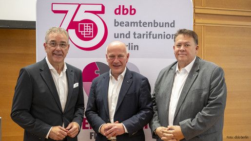 Drei Männer in Anzügen stehen vor einem Aufsteller und blicken in die Kamera