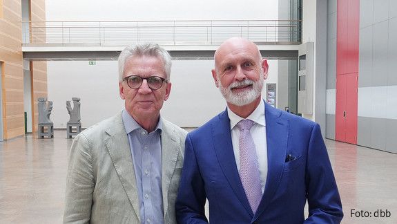 Zwei Männer in Anzügen stehen in einem Foyer und blicken in die Kamera