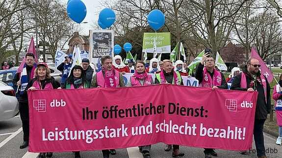Das Foto zeigt Demonstrierende in Wiesbaden am 25. März. 2026. Sie tragen Streikwesten und halten Transparente.