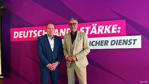 Zwei Männer in Anzügen stehen vor einer lilanen Leinwand