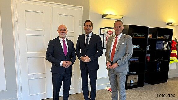 Drei Menschen in Anzügen stehen nebeneinander und blicken in die Kamera