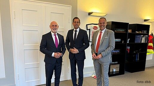 Drei Menschen in Anzügen stehen nebeneinander und blicken in die Kamera
