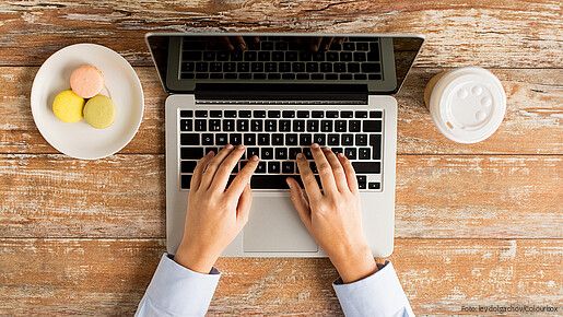 Das Foto zeigt eine Laptoptastatur, man sieht noch den Bildschirm und Finger, die auf der Tastatur tippen.