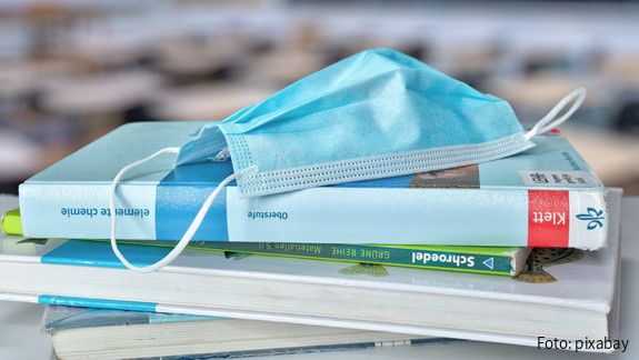Schule und Corona Stapel Schulbücher, auf dem eine medizinische Maske liegt